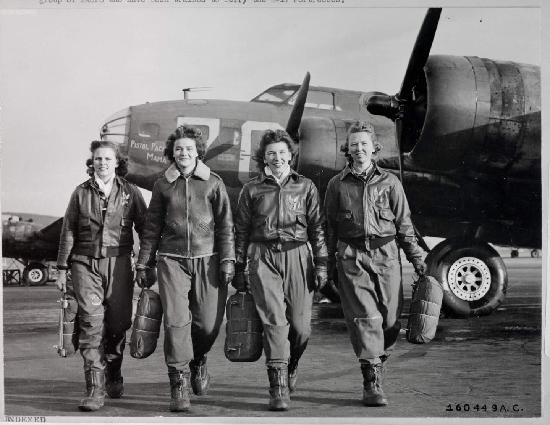 Four women in flight suits walk in front of aircraft